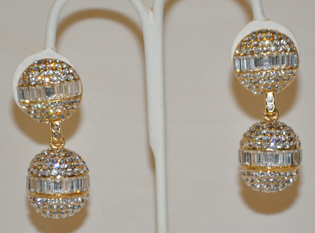 Ces boucles d'oreilles pendantes en forme de boule de cristal avec strass du lustre Christian Dior se reflètent contre les lumières dans un effet 