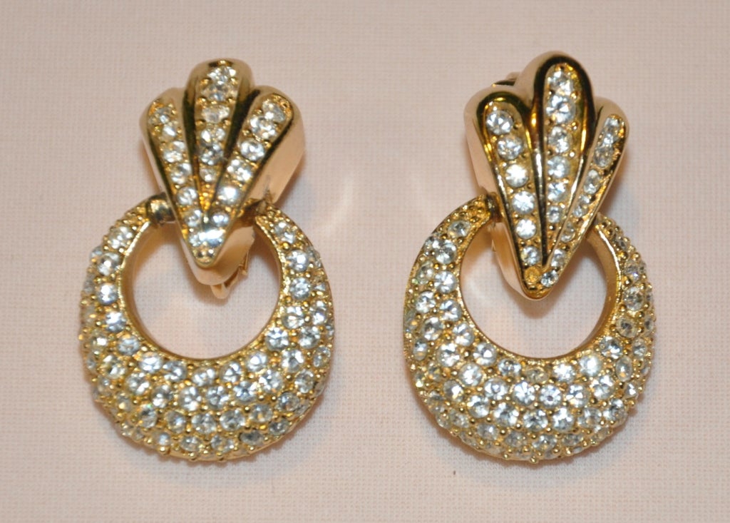 These Christian Dior earrings are in polished gilded gold hardware frame encrusted with rhinestones. The bottom of the earrings dangles. The height measures 1 1/2