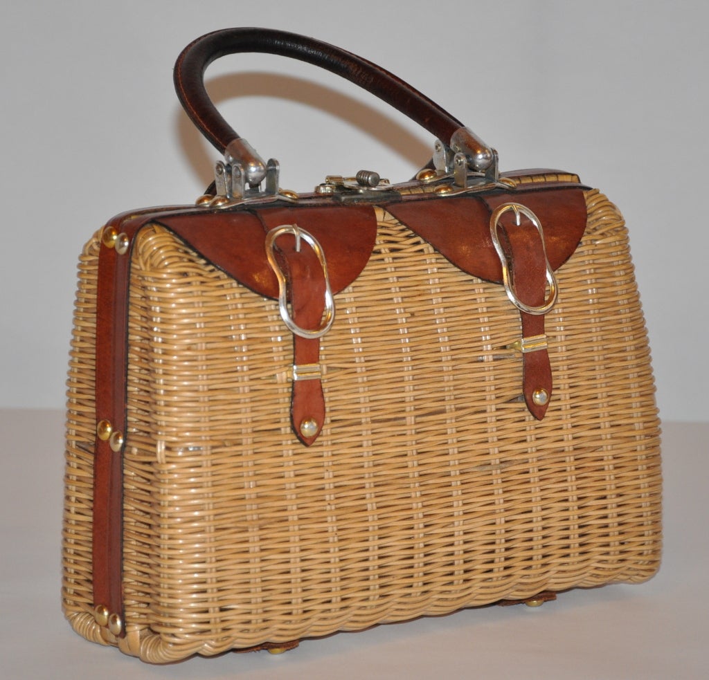 Natural-colored Wicker double-handle handbag has brown leather and gold hardware detailing. The bottom of the handbag has protective hardware, along with leather detailing also. There' an inner compartment and also an attached change purse. The