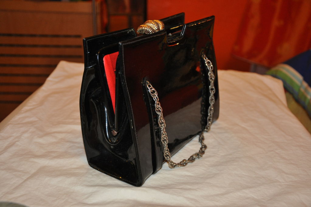 Lederer Black patent leather handbag has a red leather lining. the detailing of this wonderful handbag are gold-tone metal clasps for the opening, silver tone metal chain for handles and also for the exterior footing along the bottom of the