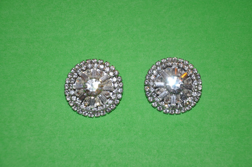 Questi orecchini a clip con strass anni '60 sono semplici ma eleganti. La pietra centrale è rotonda e circondata da pietre a forma di marquis e retangle, mentre il bordo esterno è formato da piccole pietre rotonde. Semplicemente elegante! Le pietre