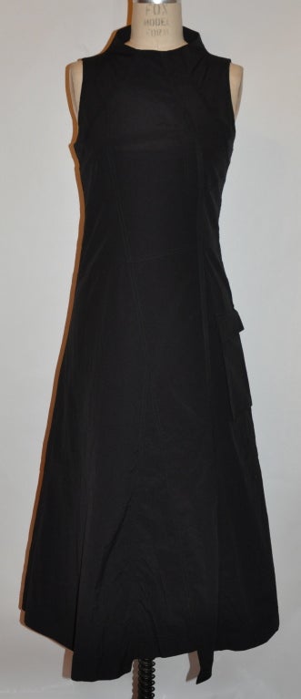 Asymmetric-styled black viscose dress is fully lined in chiffon. There's a single ribbon detail off-centered in front along with a patch pocket and a off-centered large patch pocket with flap off the hip area. 
  The back has a invisible center