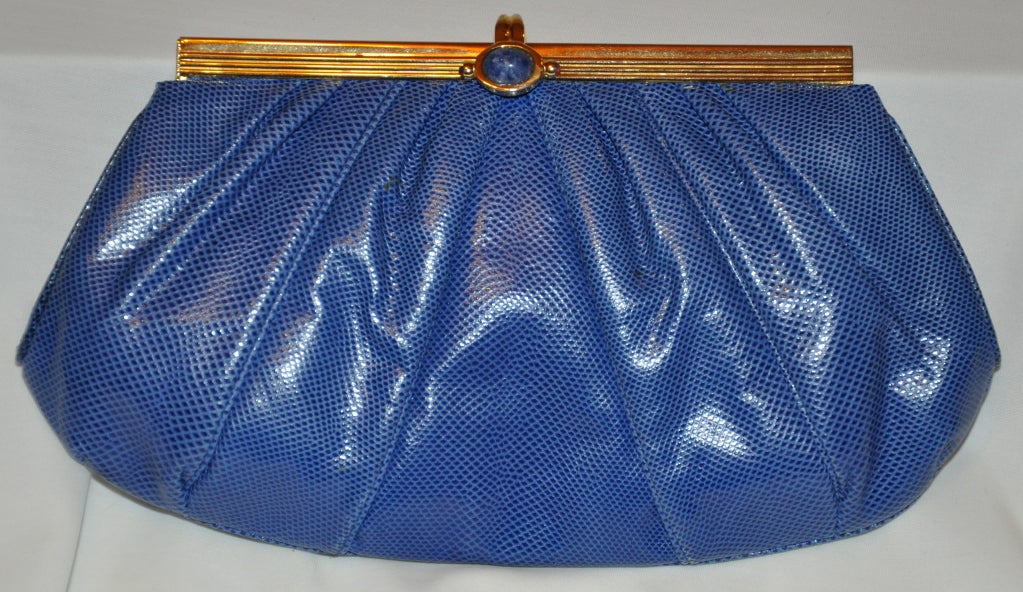 Die Judith Leiber Clutch aus blauer Eidechse hat einen goldenen Metallrahmen und ist in der Mitte mit Lapis hervorgehoben.
  Die Breite beträgt oben 6 3/4