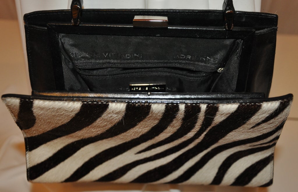 Adrienne Vittadini leather shoulder bag has a base metal frame. The pony-skin is stenciled with a zebra print and accented with black calf-skin leather around the frame along with the shoulder straps.
   The bottom of the shoulder bag has four