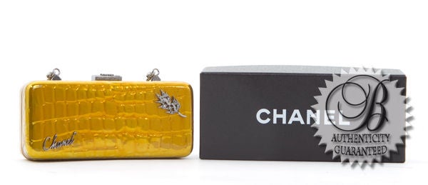 This is an authentic CHANEL Patent Gold Croc Embossed Swarovski Minaudiere Clutch Bag. It is done in croc embossed patent gold leather. This bag features Swarovski crystal detailing, a long silver chain, and Chanel logo on the front of the bag. This