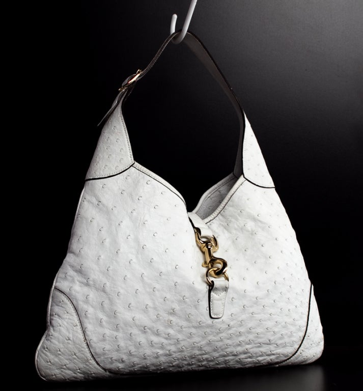 This is a preowned authentic Gucci Ostrich Skin Jackie-O Hobo bag.  Done in luxurious white ostrich skin with matching trim and chocolate brown piping, this classic hobo style is sure to glam up any outfit. It features a unique pale gold metal