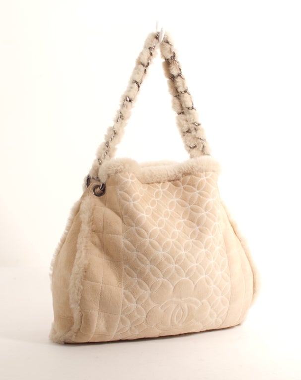 This is an authentic CHANEL Ivory Beige Quilted Leather Suede Shearling Bag. It is done in luscious beige suede and shearling. This bag features a double chain and suede shearling handle, a unique front design with the Chanel logo, snap closure and