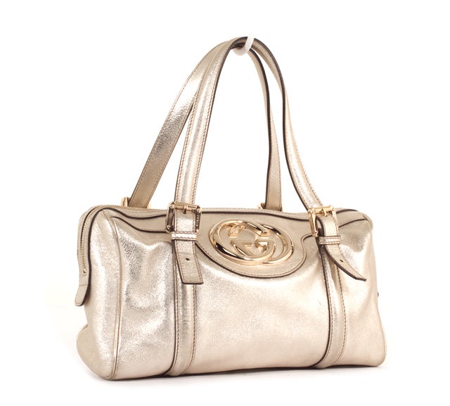 This is an authentic GUCCI Metallic Large Boston BRITT Satchel Bag. It is done in a silver metallic leather with coordinating leather trim. There are two flat handles, silver hardware with a Gucci GG hardware accent and a single zipper closure. The