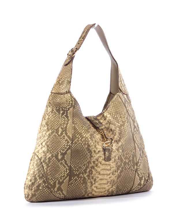 This is an authentic Gucci Beige Python Jackie O Hobo Bag. It is done in luxurious beige and caramel colored python skin with pale gold hardware and dark undertones. It featuers a single flat adjustable leather handle, as well as a flap tab with