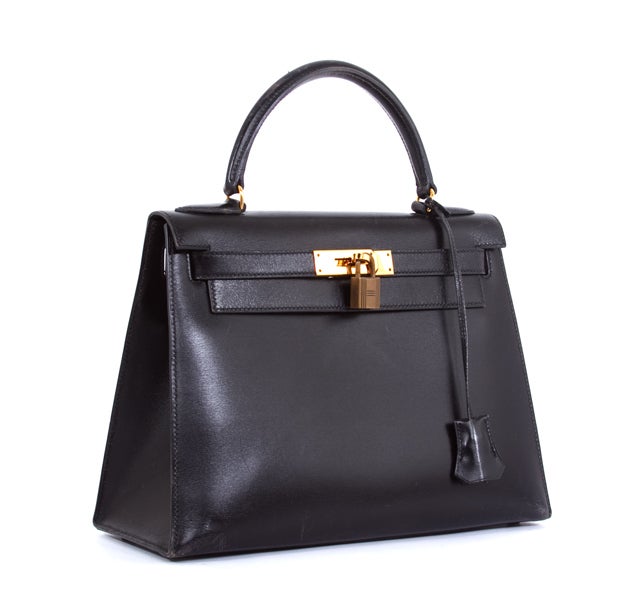 This is an authentic HERMES Black Box Calf Kelly 28 cm Purse Classic Bag. It is done in gorgeous Black leather with gold hardware. It features a single rolled leather handle and the signature Hermes flap top closure with leather strap over round