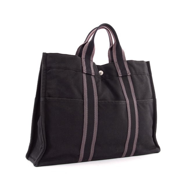 This is an authentic HERMES Black and Grey Fourre Tout MM Tote Bag. It is done in soft black canvas with grey colored accents. The bag features 6 exterior pockets, with 3 on either side. This classic style tote features two flat canvas handles and