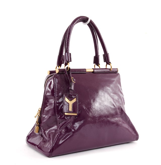 This is an authentic YSL Yves Saint Laurent Eggplant Patent Leather Rive Gauche Majorelle. The bold purple patent leather is accented with distressed gold toned hardware. The exterior features dual rolled handles, lock, keys, logo hang tag, and