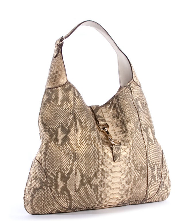 This is an authentic Gucci Beige Python Jackie O Hobo Bag. It is done in luxurious beige and caramel colored python skin with pale gold hardware and dark undertones. It featuers a single flat adjustable leather handle, as well as a flap tab with