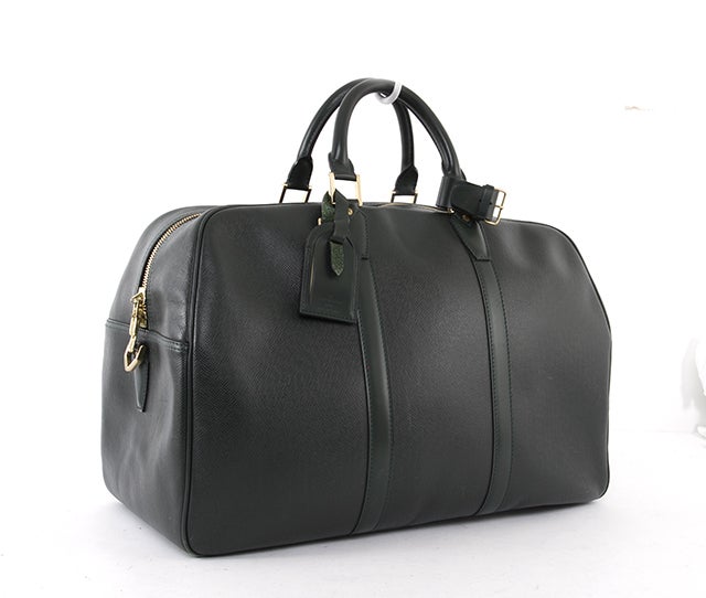 This is an authentic Louis Vuitton Kendal PM Taiga Leather Travel Bag. It is done in lovely forest green signature Louis Vuitton Taiga leather with smooth leather trim and gold tone hardware. It features a large, spacious interior with a D-ring for