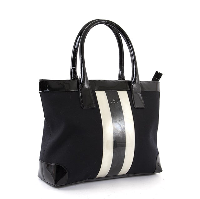 This is an authentic GUCCI Black White Patent Center Stripe Tote Bag. This traditional tote is done in lovely black canvas with patent trim. It features a white and black patent strip down the center, dual rolled patent handles, and a simple zip