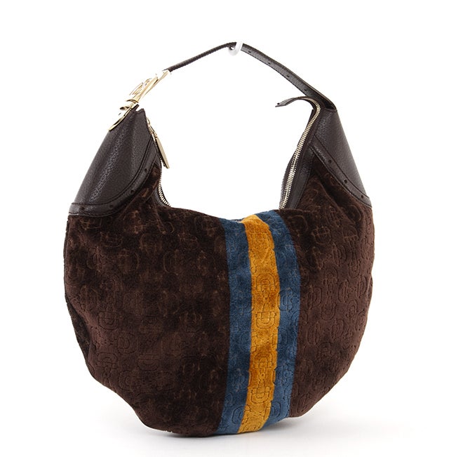 This authentic Gucci Hobo Bag is done in a unique, brown velvet abstract design with a blue and yellow stripe down the center. The flat structure features a brown leather trim, a single flat and stitched leather handle, pale gold-toned hardware, and