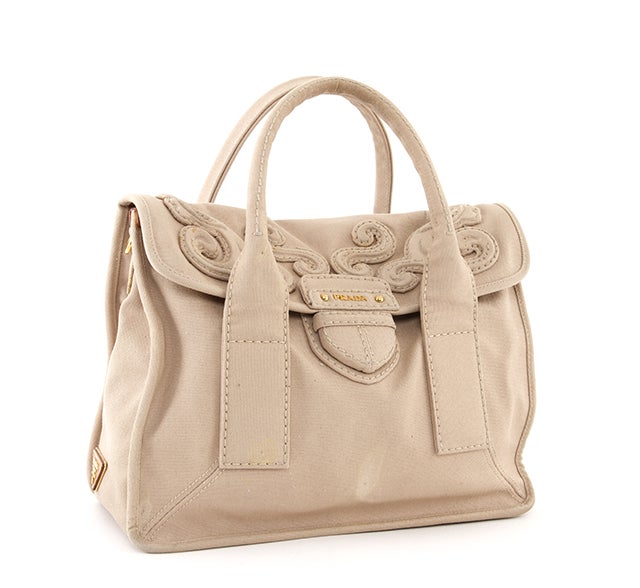 This is an authentic Prada bag. It is done in lovely beige canvas material and features stunning gold-toned hardware, two rolled handles, and a flap and closure with canvas stitched accented designs. This particular bag also includes a detachable