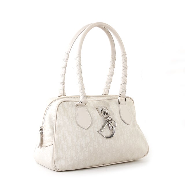 This is an authentic Dior bag. Done in cream-on-cream monogram canvas, this bag features extremely light pink leather trim, leather handles wrapped with other pieces of leather for detail and silver-toned 