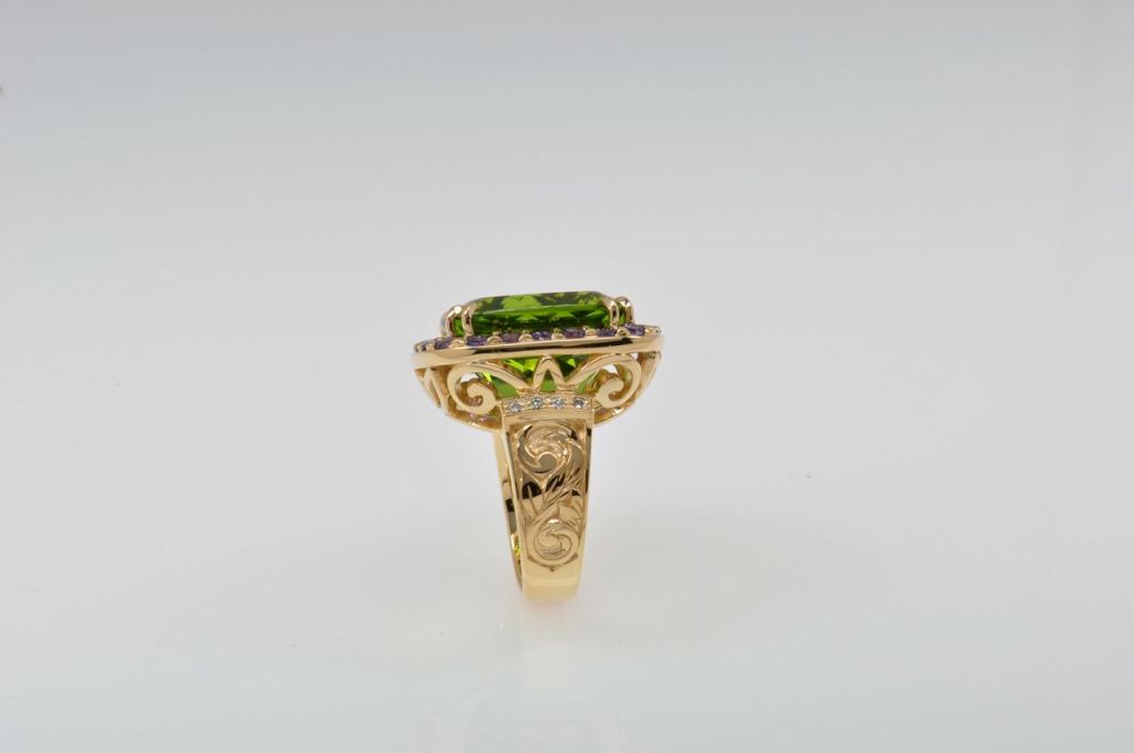One-of-a-kind, hand-carved ring featuring 24.0 carat Pakistani Peridot center-stone, 2.58 carats of unheated purple Sapphire, 0.35 carats of Diamond, and 20.39 grams of 18K Yellow Gold. Hand-carved engraving on the sides of the shank.  An amazing