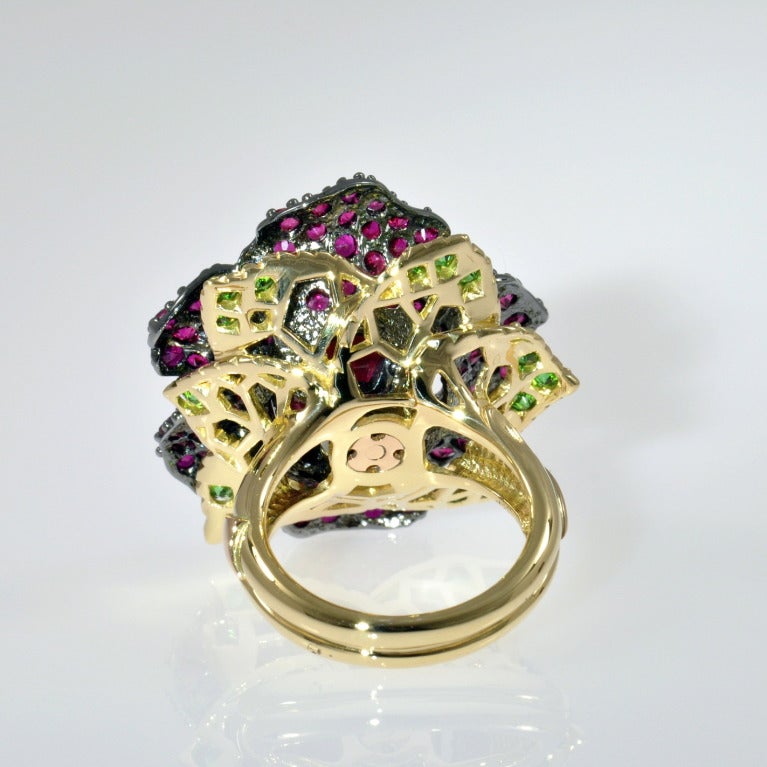 Featuring an oval cut 7.04 ct Burmese Ruby surrounded by 4.90 carats of Ruby melée and 0.74 ct of Tsavorite Garnet melée in 18K Rose & 18K Green gold, with black Rhodium plating.  Entirely hand-carved and made by the lost wax process.  Heat is the