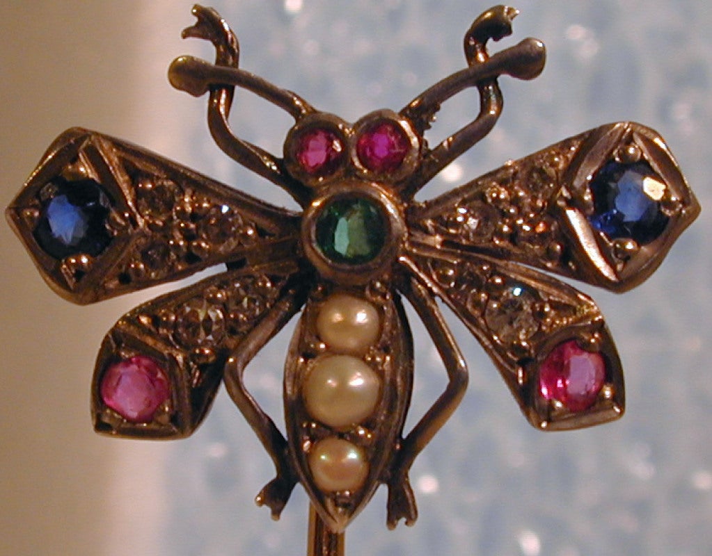 Fluttering gem set butterfly stickpin will brighten any lapel or scarf. Set with rose diamonds, rubies, sapphires, pearls and an emerald this bright beauty will liven up your day. The pin is 2