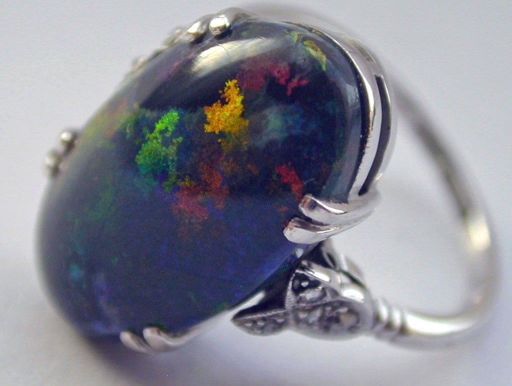 Splashing colors, ever changing, define this wonderful black opal ring set in 18K white gold with diamonds. The stone weighs 6.25 cts.  Glorious in daylight and magical by candlelight. The ring size is a 6.