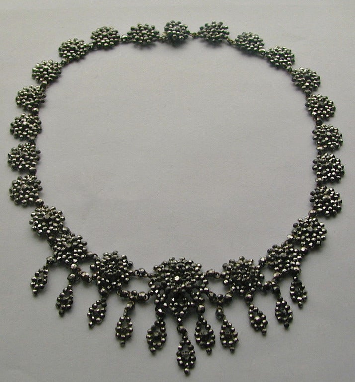 Floral rondelles, the five central ones with tassels, comprise this lovely cut steel necklace. Multi-faceted cut steel jewelry was popular during the 18th and mid 19th century.  The jewelry sparkled in candlelight and was used as a substitute for