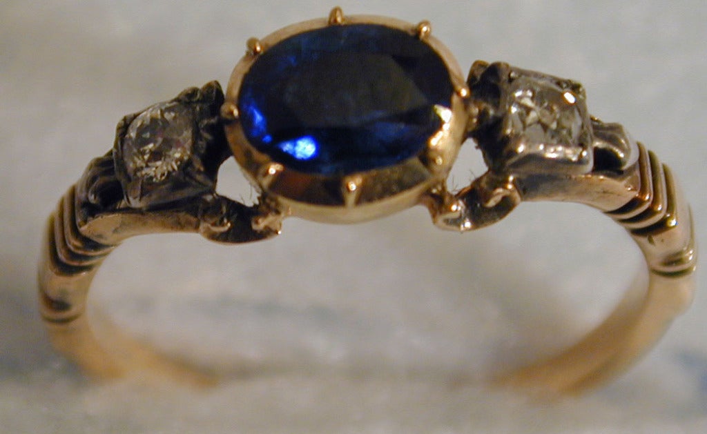 Georgian sapphire ring flanked by two cushion cut diamonds in a classic 15K yellow gold setting. These early rings were typically worn with several other rings, often one on every finger. This ring is a size 7 and can be resized. It measures
