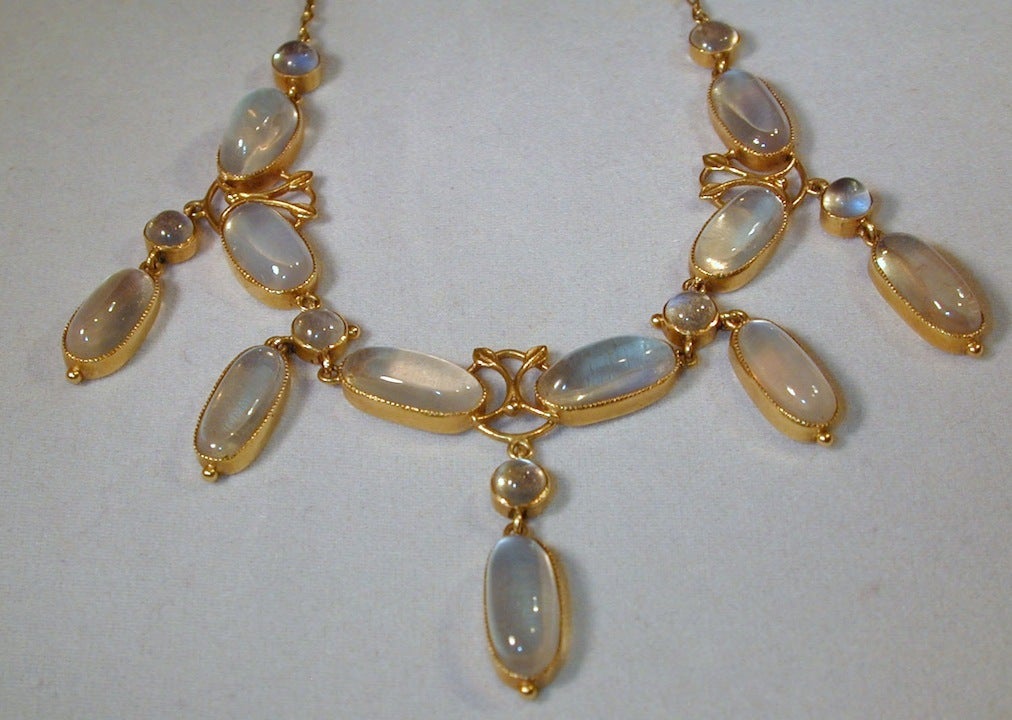 Expertly crafted by the well known Arts and Crafts jeweler, Liberty & Company, this moonstone necklace with round and oval cabochon stones is set in 18K gold. The gold beads at the end of the drops and the leaf motif between the stones add an