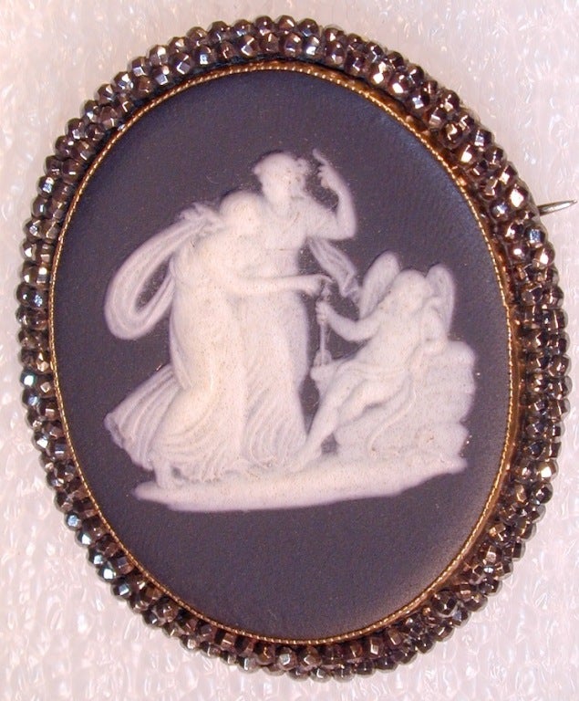 Classical Wedgwood black jasper brooch set in a cut steel bezel. The sparkling border highlights the scene of two elegant ladies who seem to be chastising a reluctant cupid.