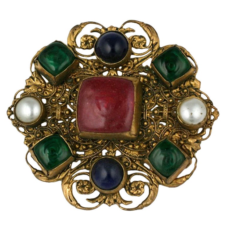 Large, early crest brooch of pate de verre cabochons set into an ornate filigreed base by Robert Goossens for Chanel.
Displaying her love for the baroque, Chanel choses flawed ruby, emerald, deep sapphire and faux pearl pate de verre 