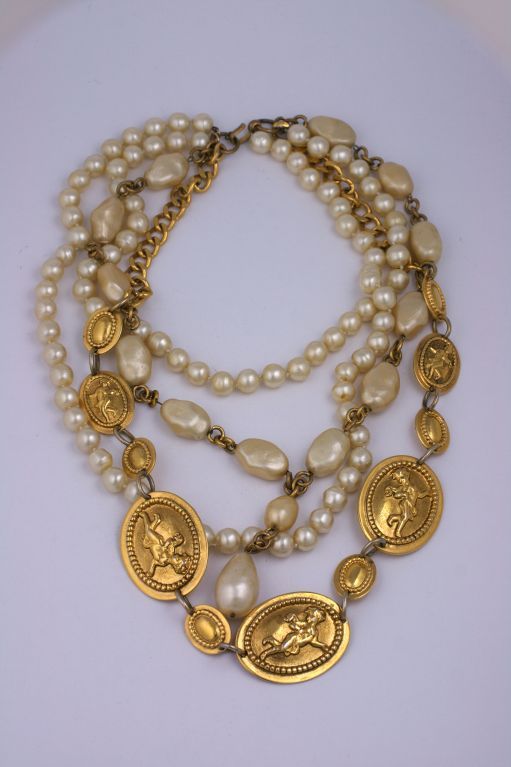 Massive bib with multiple strands of hand made faux baroque pearls of varying sizes mixed with graduated gilt bronze cupid plaques and chains. 

Based on a famous Chanel necklace created in the 1930s, this supersized version was created by Maison