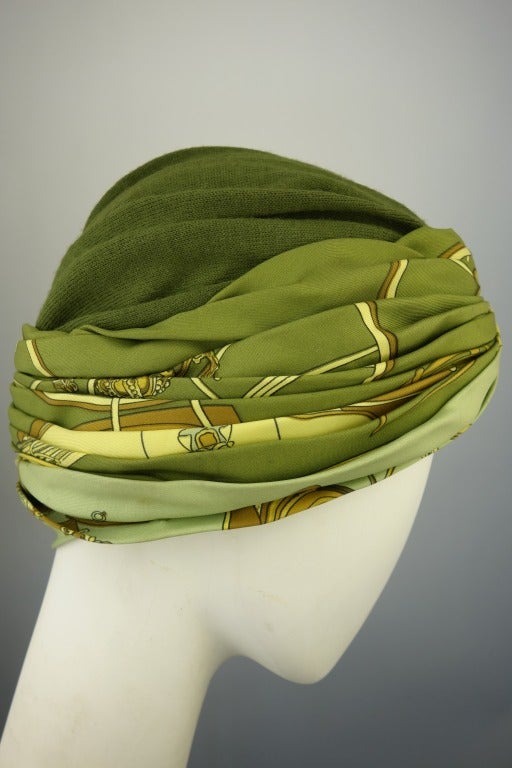 Hermes olive green wool jersey turban with silk printed band.

Circumference: 23