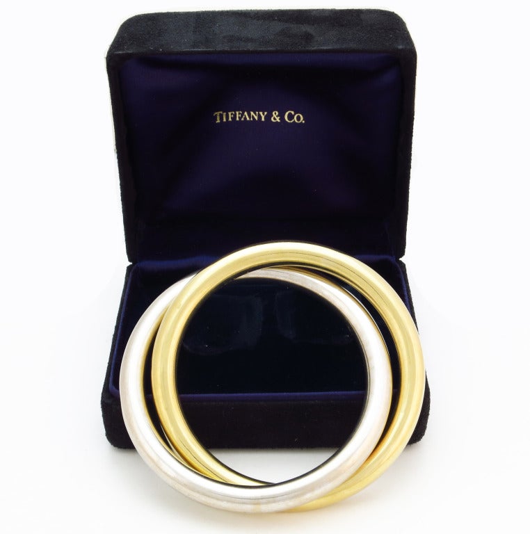 Featuring a pair of 18K yellow and white gold interlocking bangles. Signed Tiffany & Co. Each bangle has 2 9/16