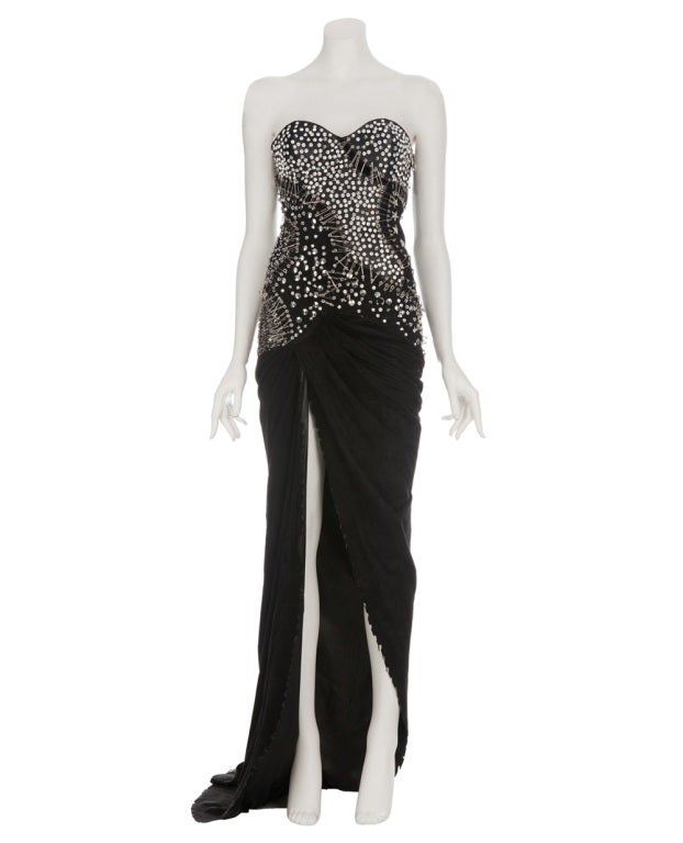 BALMAIN GOWN
Black leather bustier evening gown from Balmain featuring gathering to the skirt at the front, a slit to the front and a train. The bustier section is embellished in silver tone studs, crystal details and safety pin details.
100%