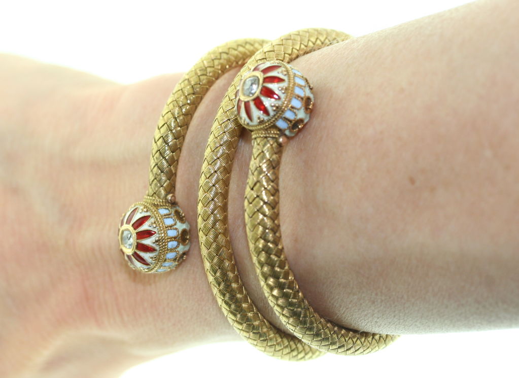 A very stylish antique coiled bracelet of woven gold with enamel and diamond terminal ends designed as floral motifs with center faceted diamonds. The goldwork on the ends is of a twisted and beaded nature and borders the crimson red, pale blue and
