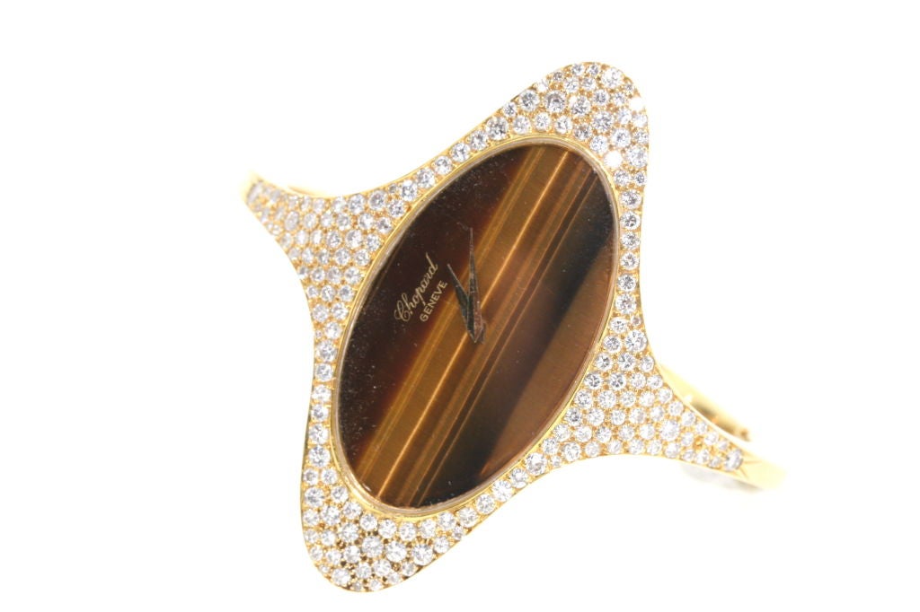 A rare 1970s 18k gold bracelet watch designed as an elliptical face of tiger eye stone surrounded by diamonds. Watch unclasps in the rear. Manual winding original mechanism. These yellow gold and hard stone watches were primarily made in the
