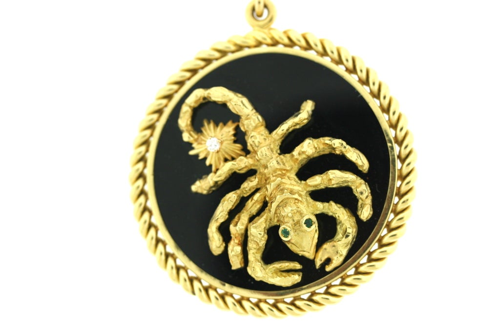 Van Cleef & Arpels 18k gold zodiac medallion in the sign of Scorpio mounted on black onyx with one diamond on the tip of the tail and two emerald eyes. Two gold stars are mounted to the reverse side of the medallion. Attached bale is signed VCA