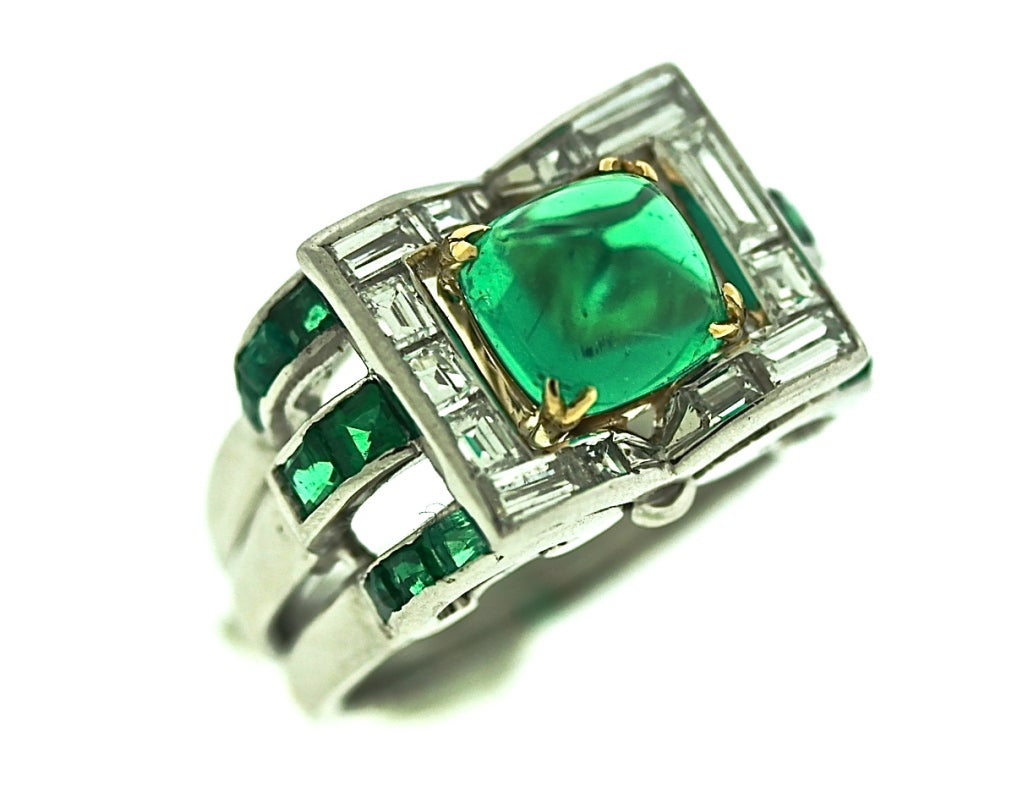 A wonderfully designed art deco emerald and diamond ring set in platinum featuring a center sugar loaf emerald of exceptional clarity and quality weighing approximately 2 carats. The emerald is surrounded by various sizes of emerald cut diamonds
