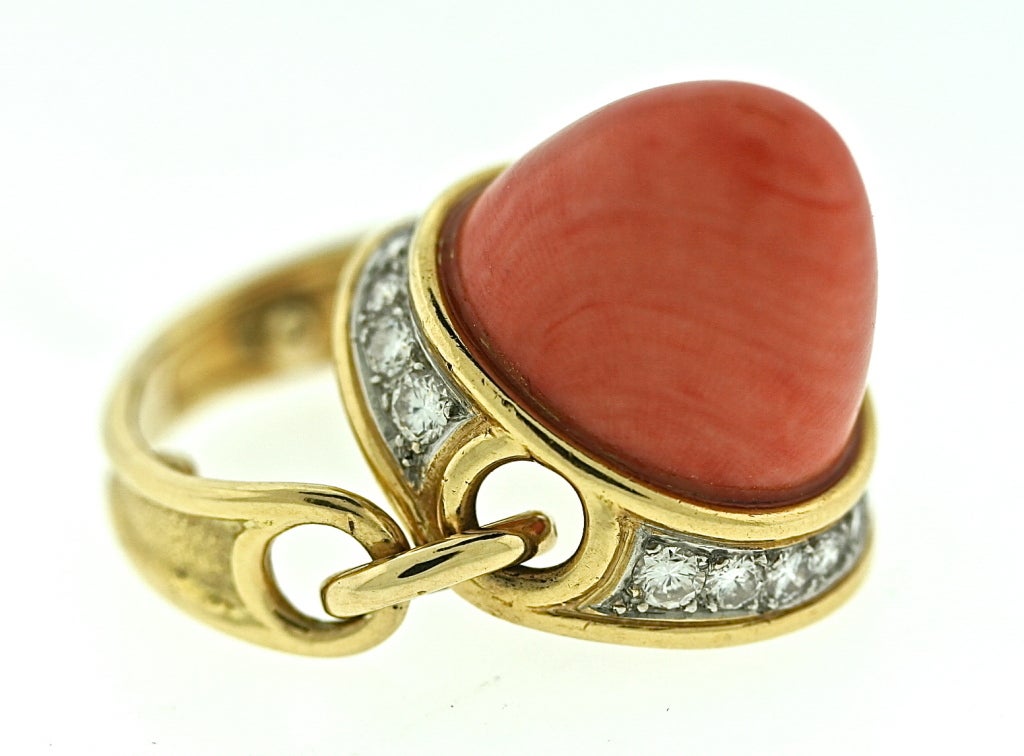 An 18k gold ring by Marvin Schluger with a large center polished coral stone surrounded at its base by 16 diamonds in a setting that contains 