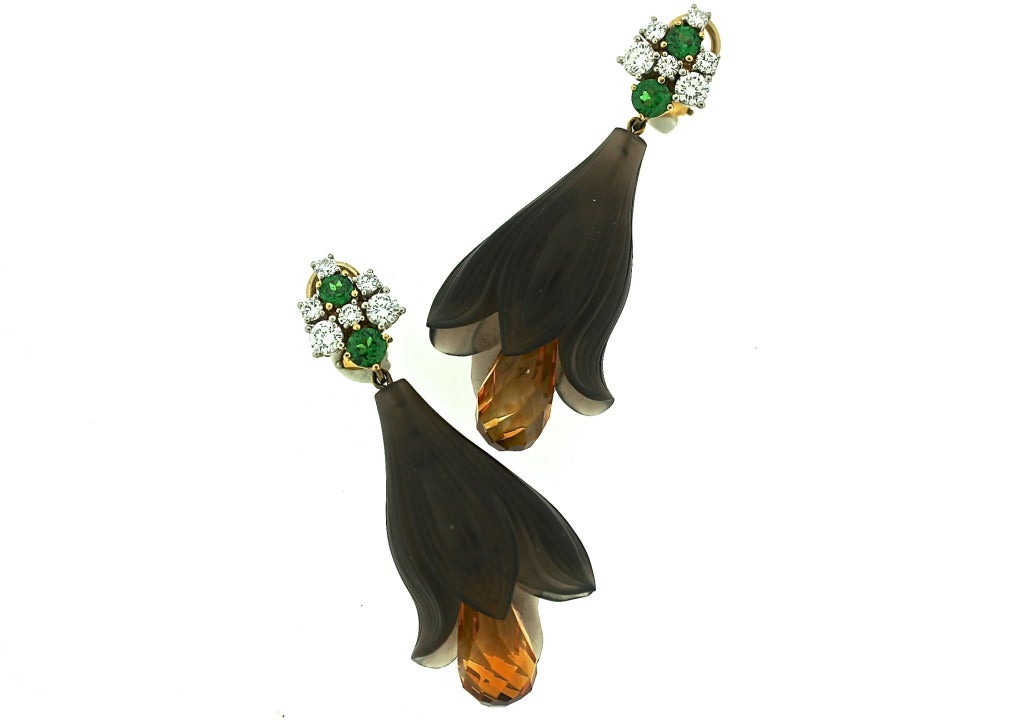 A very fine pair of 18k gold earrings designed as a dangling, hand-carved topaz flower with a moveable and faceted citrine briolette center drop. The earring tops are punctuated by platinum-set tsavorite garnets and diamonds. They were created by