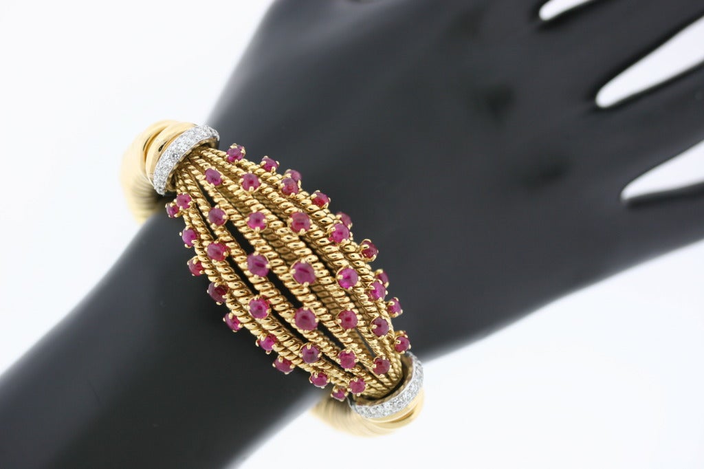 An opulent French 18k gold bracelet designed as a series of flexible interlocking links with a center twisted gold and cabochon ruby cage flanked by diamond-set platinum shoulders. A very glamorous piece reminiscent of old Hollywood. French assay