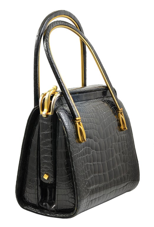 Gorgeous Judith Leiber black baby alligator handbag with gold hardware. Hard frame with alligator covered handles makes this the perfect day to evening bag. Buckle motif accents at base of handles and closure. 3 inside compartments.  Measures 6.5