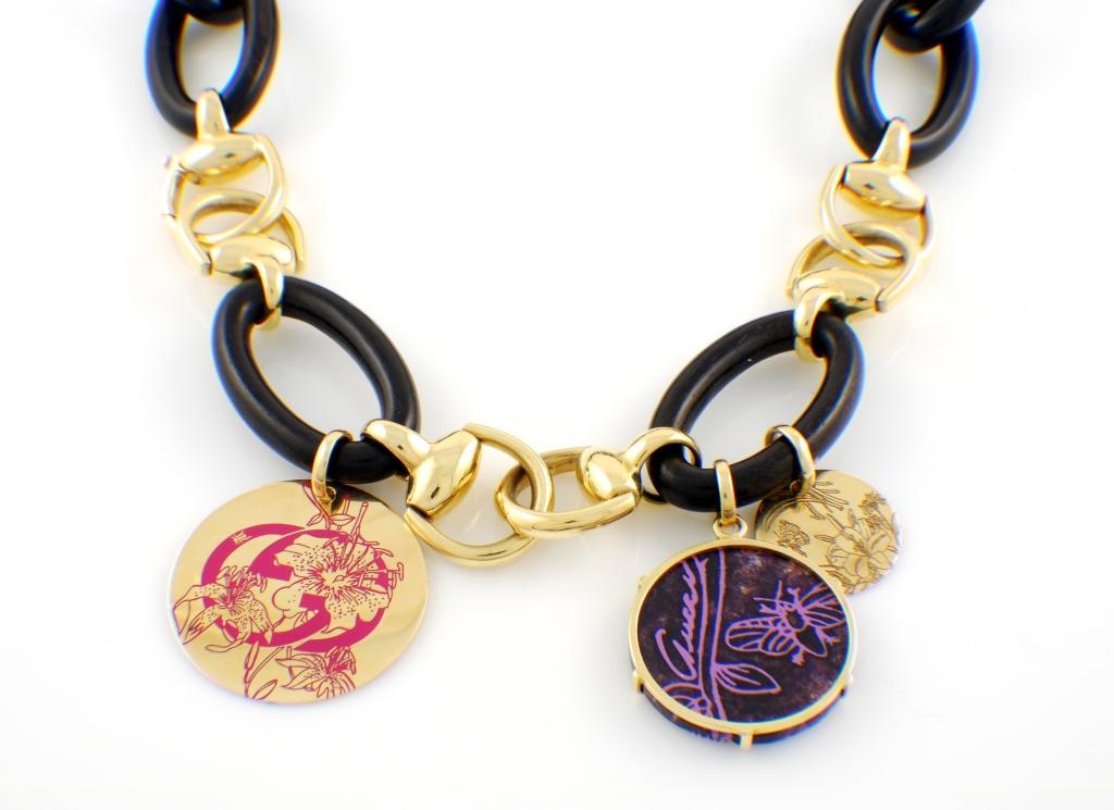 Authentic 18kt yellow gold and ebony Gucci Necklace called Flora. Features three charms, each done in high detail: a large charm with pink enamel GG logo, a purple Sugilite and a small gold flora charm. All the charms are double sided. Clasp stamped