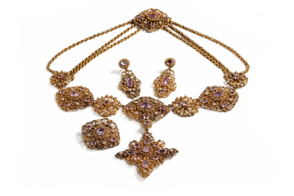 18k gold cannetille, pearls, and natural pink topaz parure features a pair of earrings, a necklace, a brooch, and a pendant that can be removed and worn as a brooch. All pieces are presented together in a fitted box.  The box was fitted to the piece