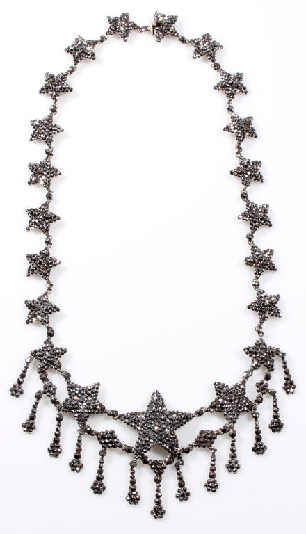 Early 19th Century Cut steel necklace in a graduated star motif. I have seen pieces like this referred to as 'Milky Way' necklaces.   Beautifully preserved with a bright gray sparkle. Most likely English in Origin. 

Steel Jewelry was introduced