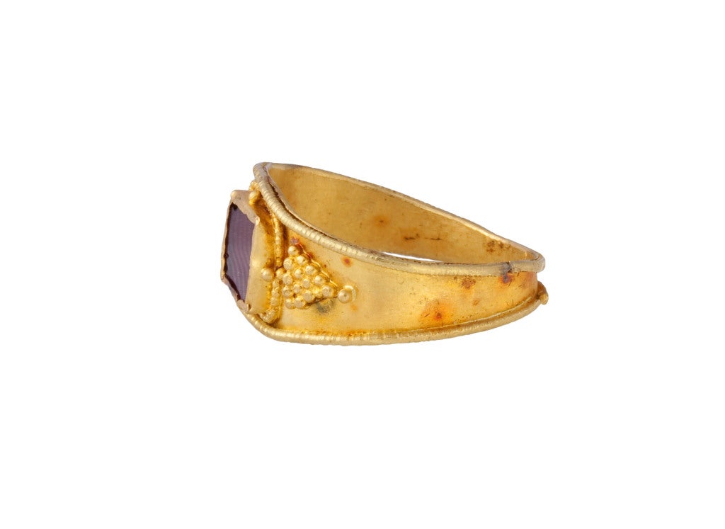 Circumference 59.5 mm.; weight 3.6 gr.; US size 9; UK size R 1/2

This ring displays features that are typical of Merovingian finger rings, such as the clusters of gold globules arranged in a triangle at the shoulders, the square-shaped gem, and