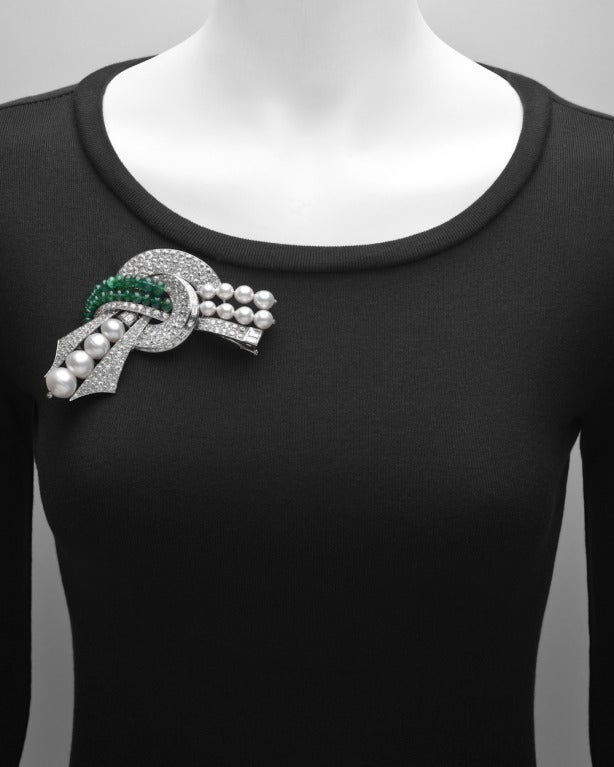 Gem-set scroll bow brooch, set with pavé circular-cut diamonds and baguette-cut diamonds weighing approximately 24.70 total carats, accented by two curving rows of emerald beads weighing approximately 20.00 total carats, and graduated rows of