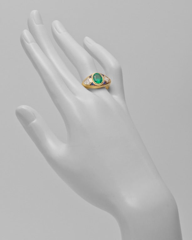 Gypsy-set emerald ring, centering on an oval-shaped emerald weighing approximately 1.97 carats, flanked by two kite-shaped diamonds weighing approximately 1.40 total carats, with four small trillion-cut sapphire accents, mounted in 18k yellow gold.