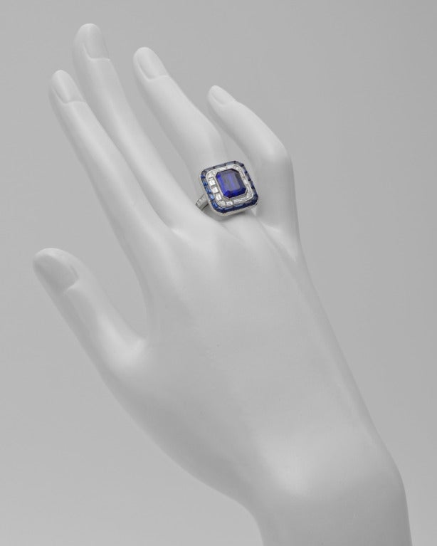 Sapphire and diamond panel ring, centering on a cut-cornered, rectangular-cut sapphire weighing 4.85 carats, within a baguette-cut diamond surround trimmed with calibre-cut sapphires, the shoulders set with baguette-cut diamonds, mounted in